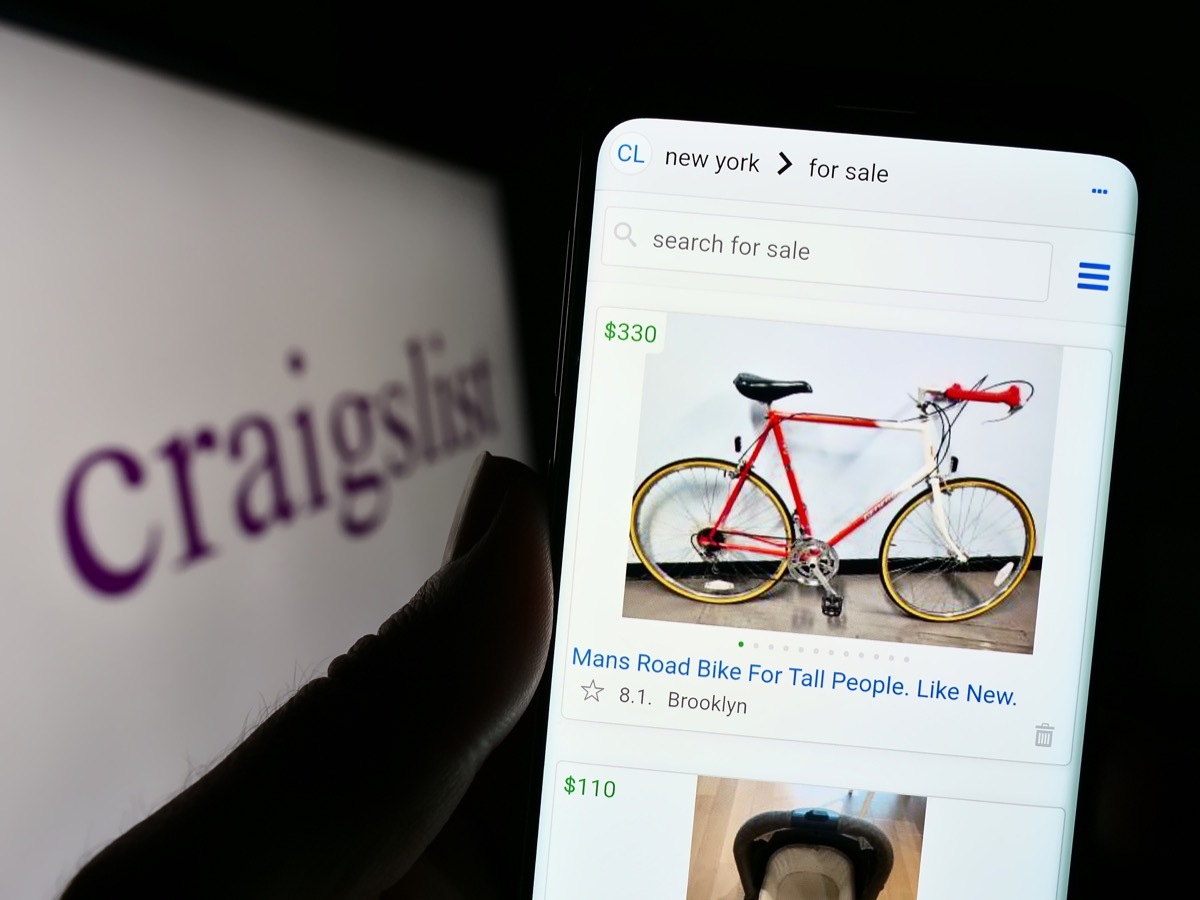 Person holding cellphone with webpage of classified advertisements company Craigslist Inc. on screen with logo. Focus on center of phone display. Unmodified photo.