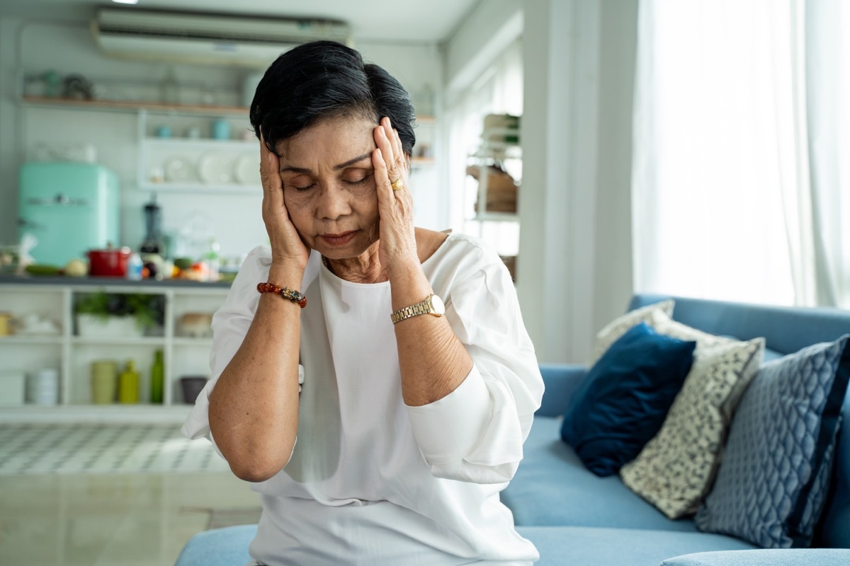 ady with closed eyes rubbing nose while sitting on sofa and suffering from headache in cozy living room at home