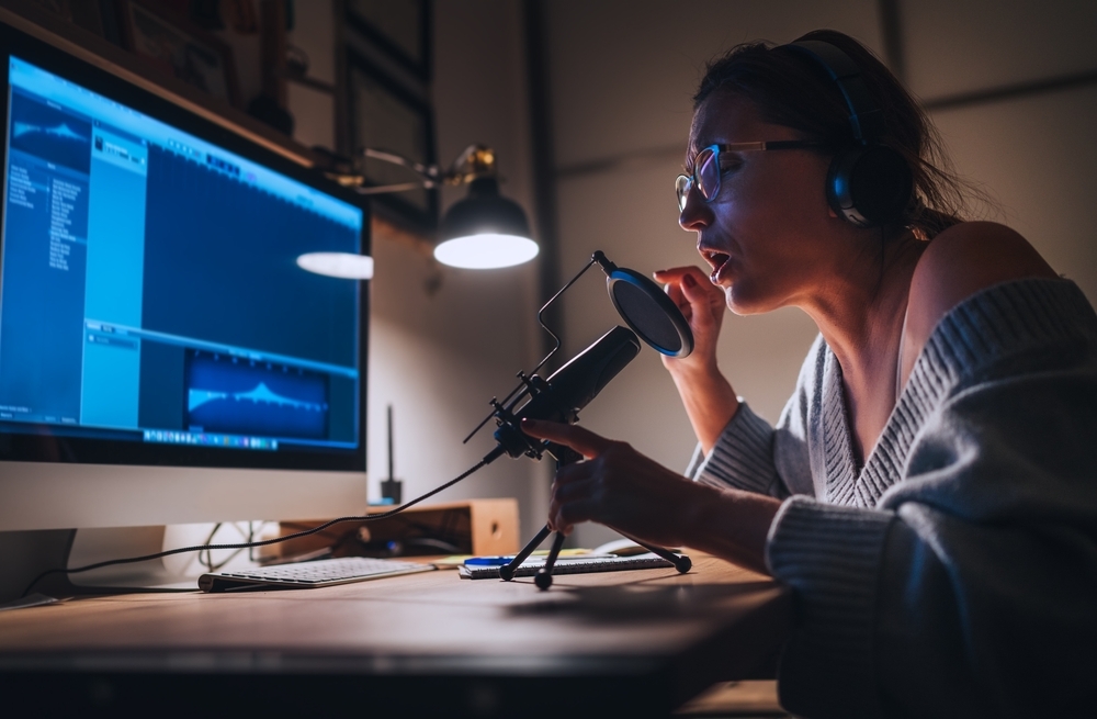 A young woman recording her voice on a computer using a microphone and headphones