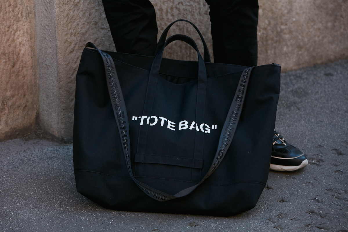 Close up of a black tote bag at a man's feet with the words 