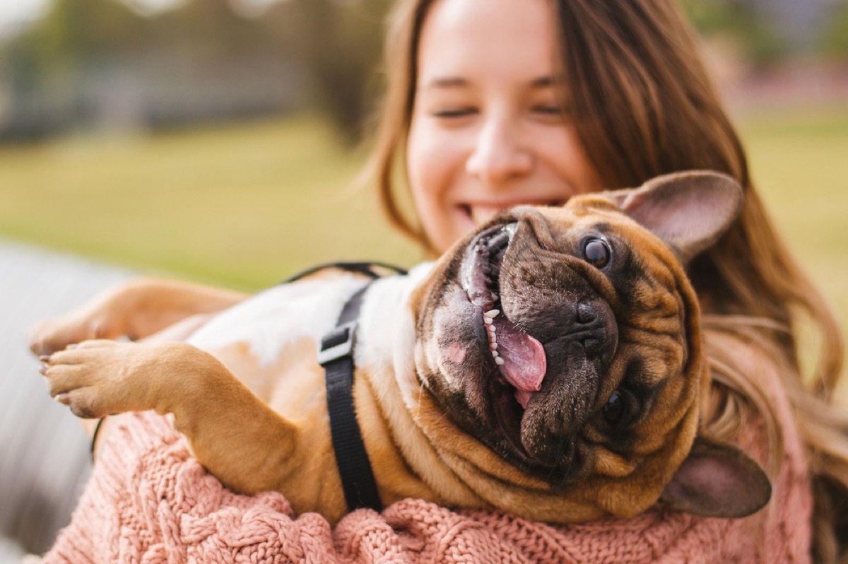 young woman smiling while holding a little dog outside