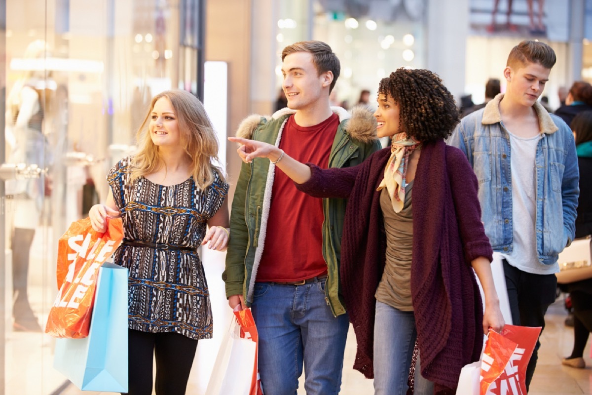 group of young friends carrying bags and pointing at a window at the mall