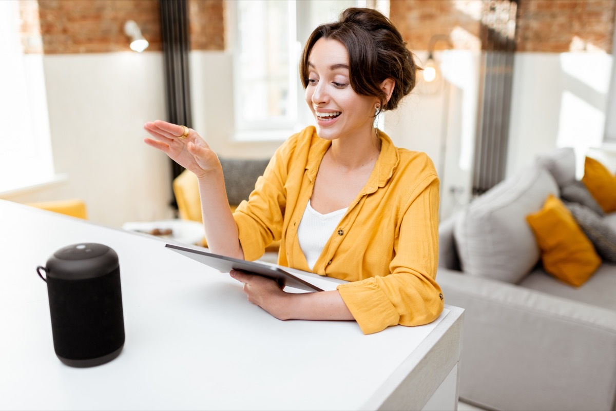 Happy young woman controlling smart home devices with a voice commands and smart speaker at home. Concept of a smart home and managing wireless devices remotely