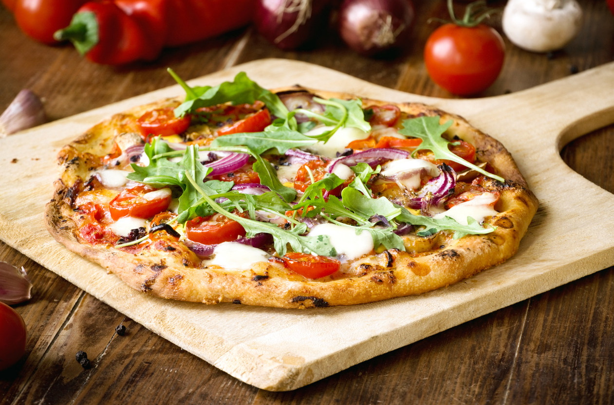 Freshly baked pizza with arugula, tomato, red onion and mozzarella