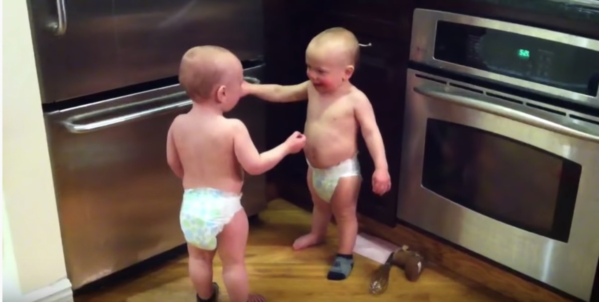 twin babies in diapers in kitchen talking to one another