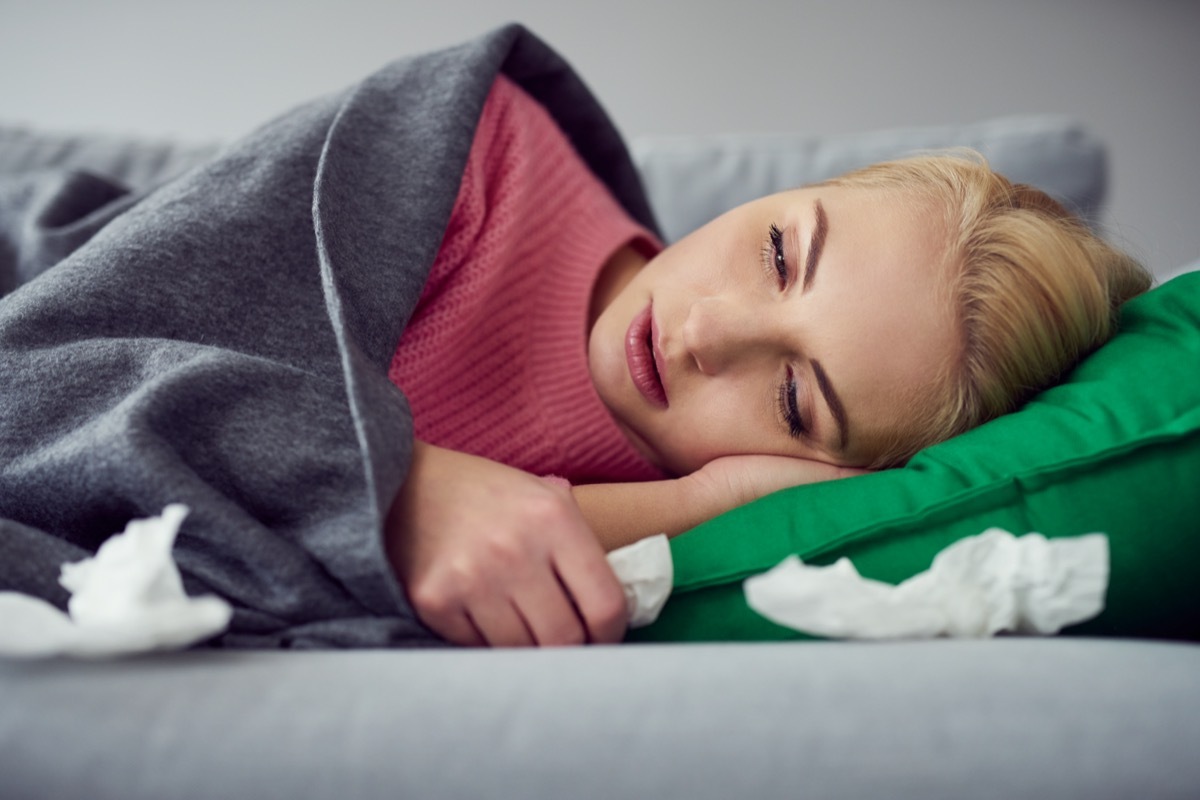 Woman suffering from cold, virus lying on the sofa under the blanket