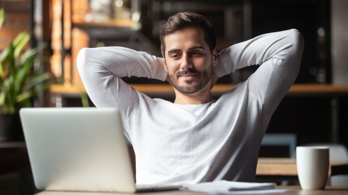 Young Man looking at laptop screen, leaning back with his hands behind his head