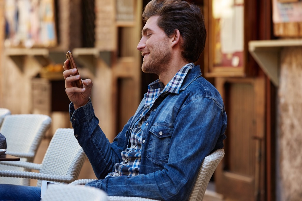 man at outside cafe on his phone, The best opening lines for online dating