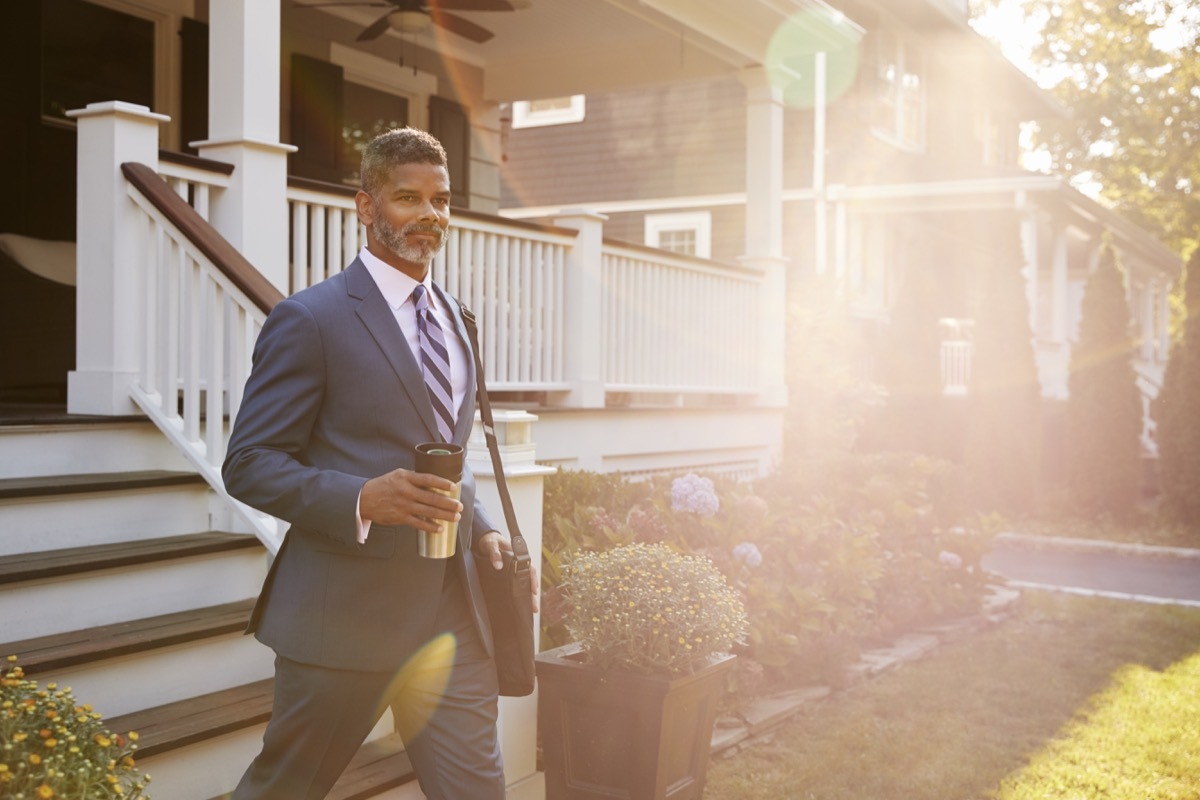 Businessman With Cup Of Coffee Leaving Suburban House For Work