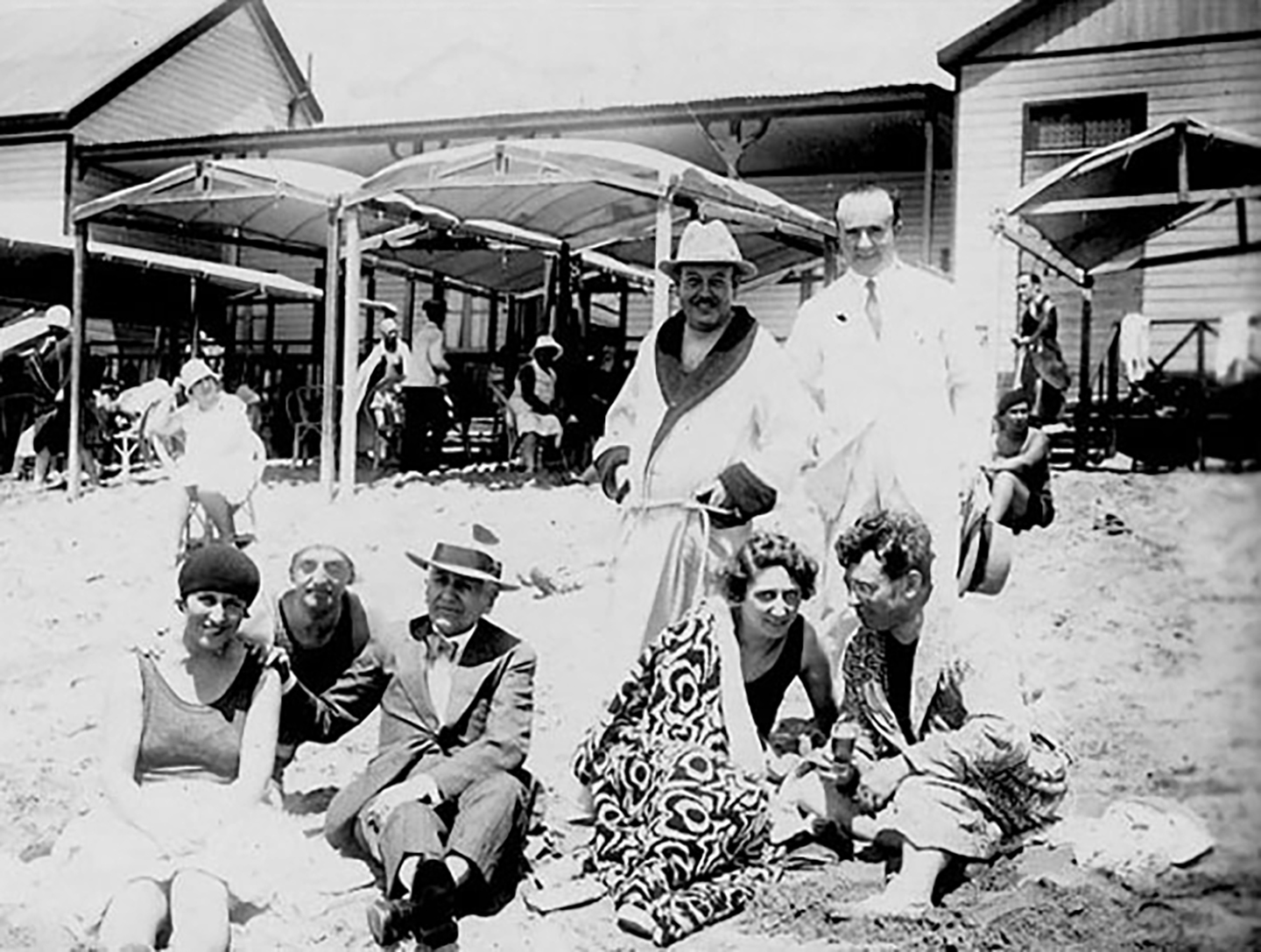 a group of men and women pose on a beach in the 1930s