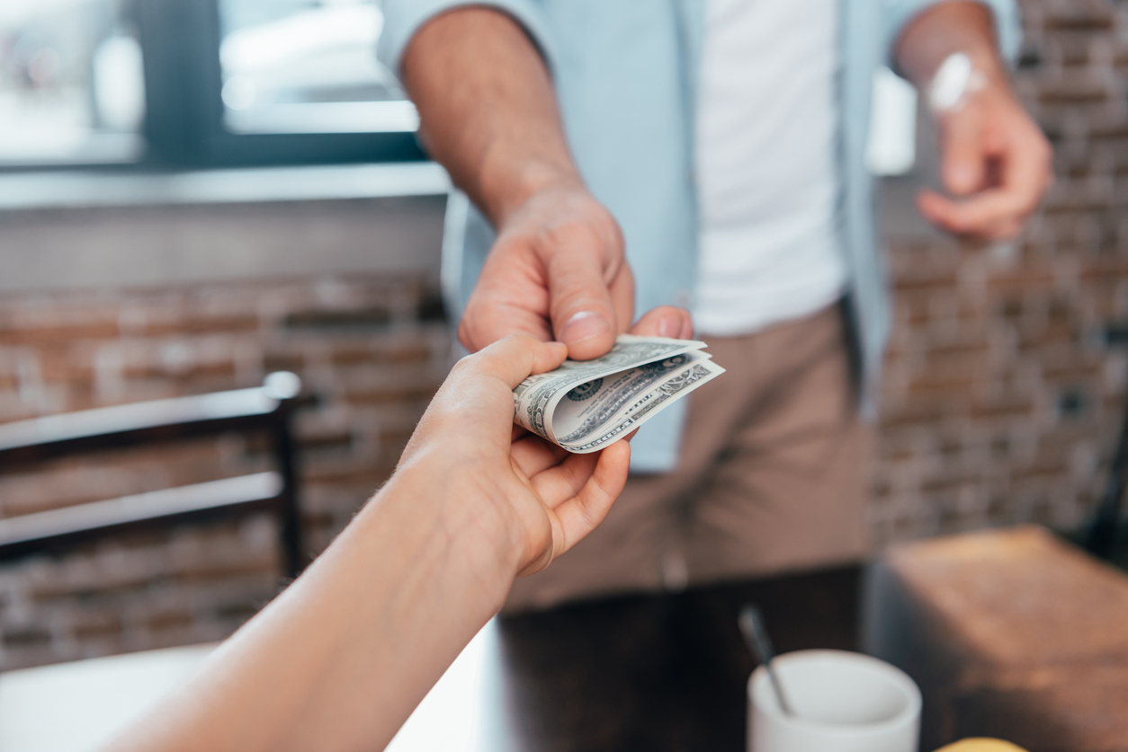 Close up of someone handing a person dollar bills