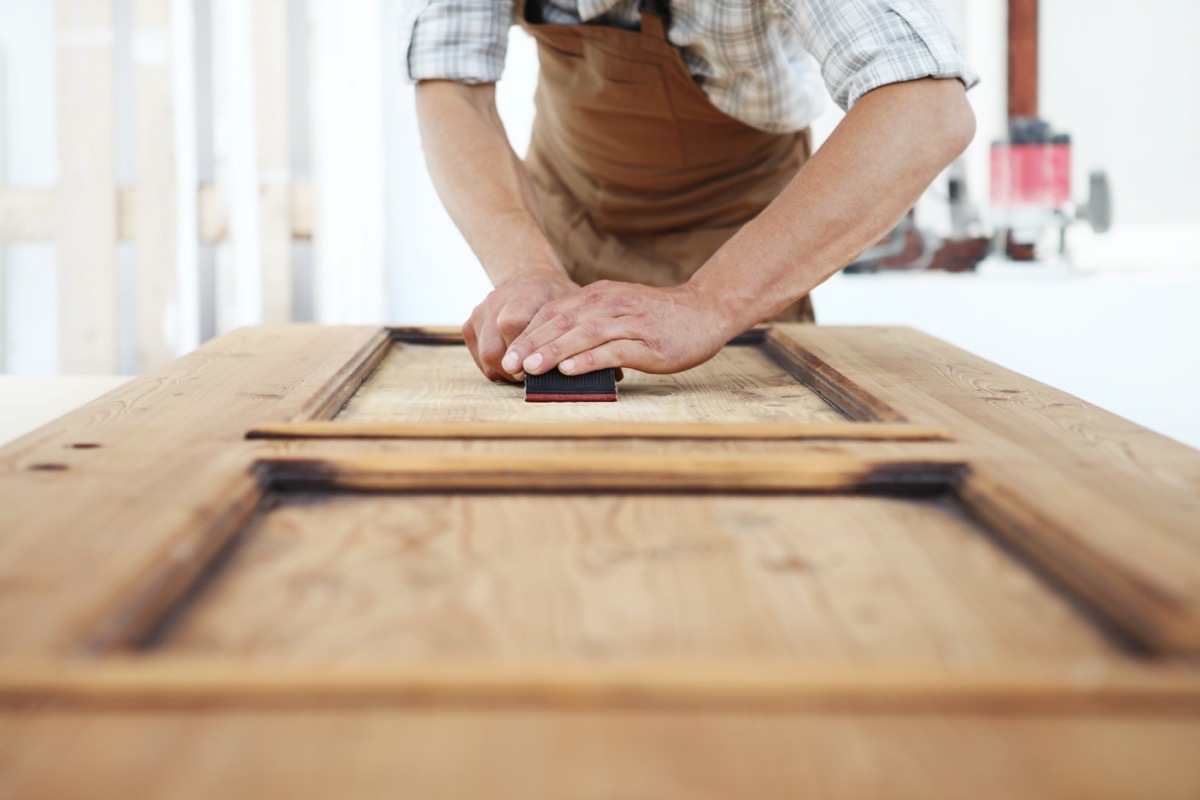 white man sanding wooden door