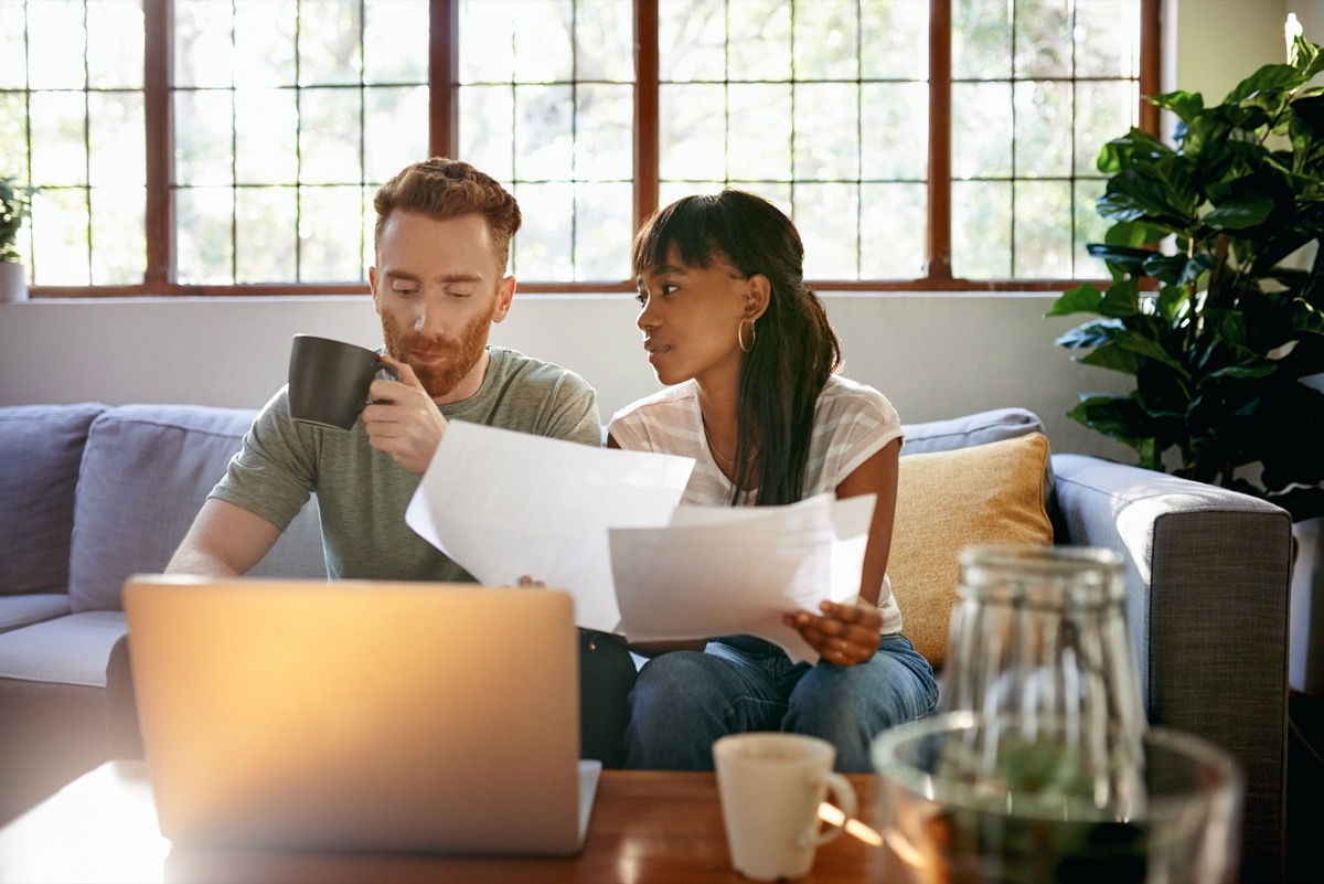 Shot of a young couple going through paperwork while using a laptop at home