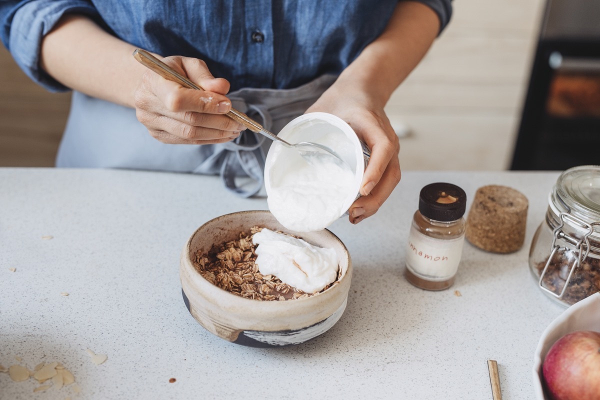 Making breakfast: unrecognizable woman adding yoghurt to oatmeal.