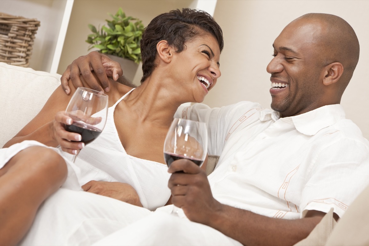 couple sitting at home together laughing and drinking glasses of red wine