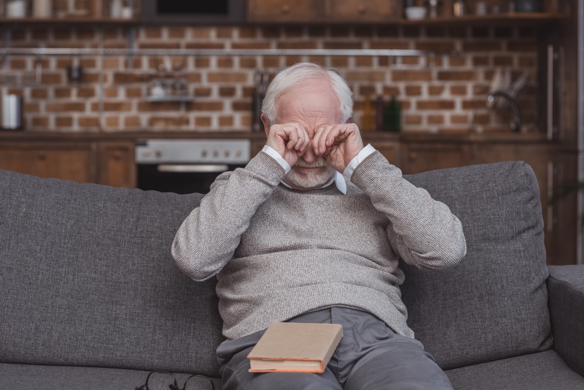 older man rubbing his eyes on the couch