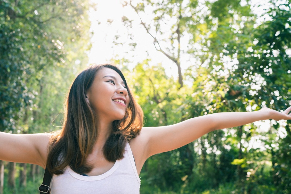 young asian woman with her arms out in a forest