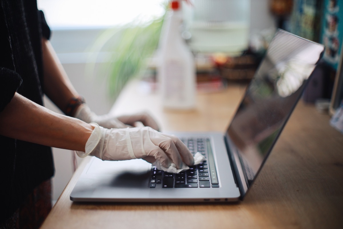 Woman is sanitising her laptop surface agains viruses and germs in midst of the coronavirus - covid19 worldwide outbreak.