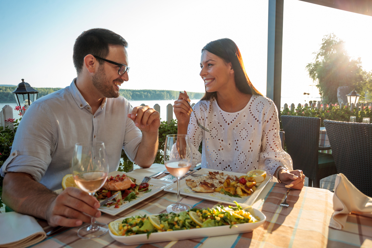 Beautiful happy young couple making a toast, celebrating anniversary or birthday in a restaurant. Husband and wife having romantic dinner in a restaurant by the river