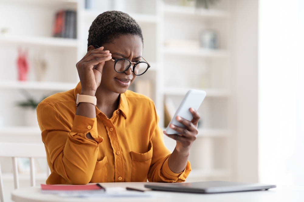 A young woman looking at her phone with a confused look on her face after receiving a text message