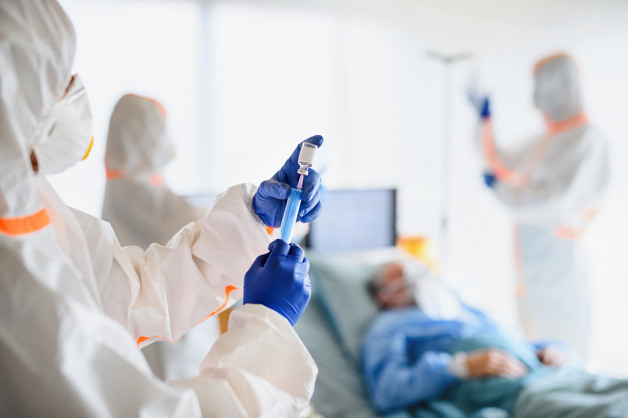 A health care worker wearing full protective gear prepares to inject a patient with a coronavirus vaccine.