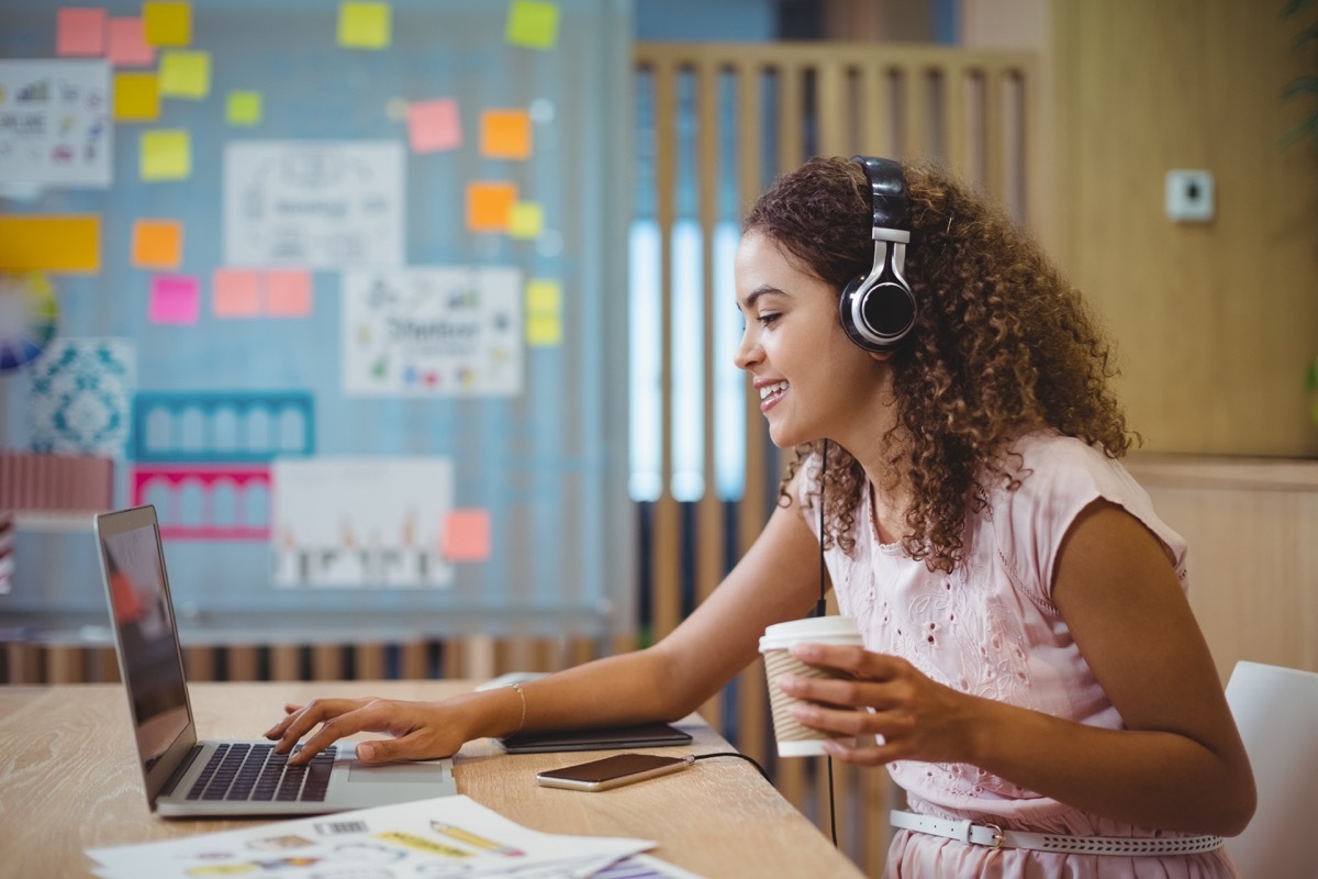 Female graphic designer listening song while using laptop in office