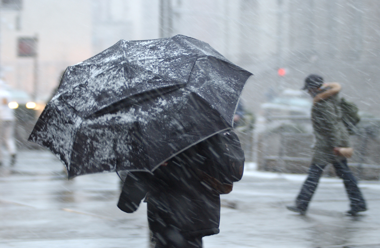 A pedestrian walking in a snowstorm with an umbrella