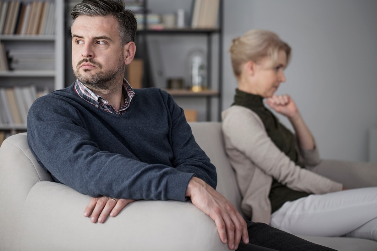 Men and woman sitting on a white sofa separately after a fight