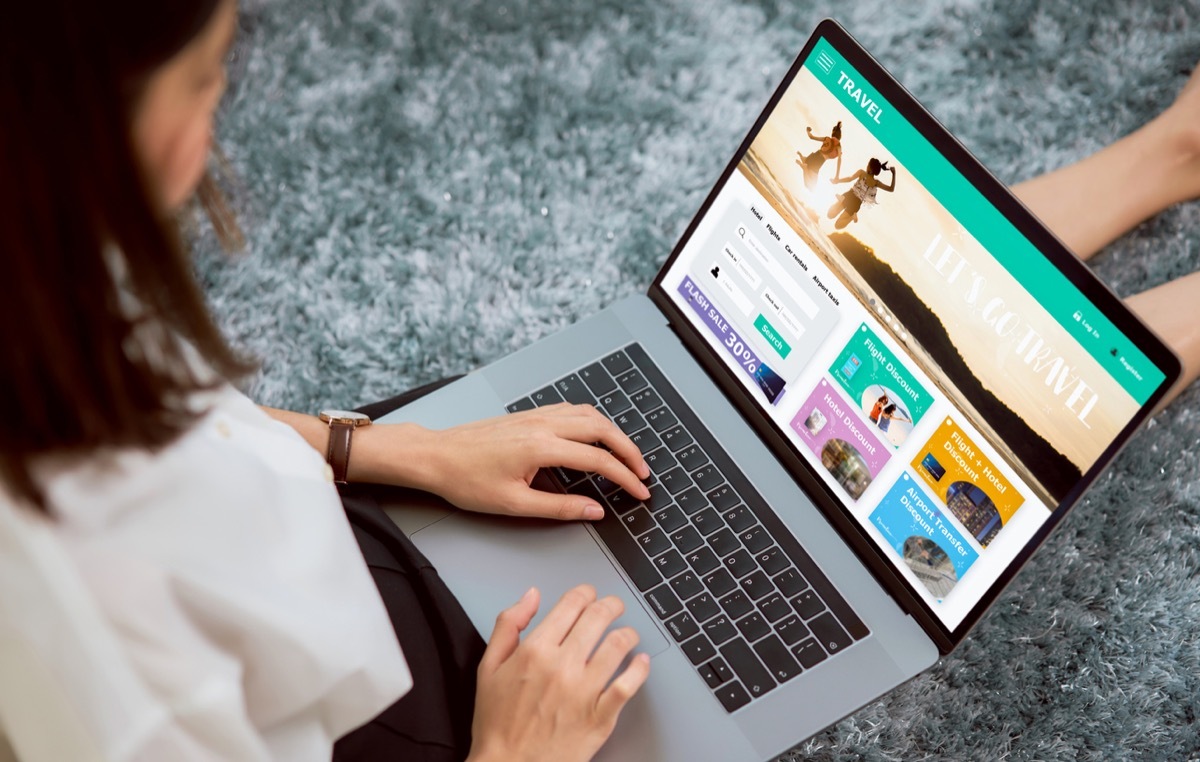 woman sitting on floor with laptop in her lap, looking at a travel booking site.