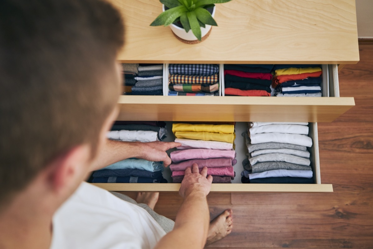 Organizing and cleaning home. Man preparing orderly folded t-shirts in drawer.