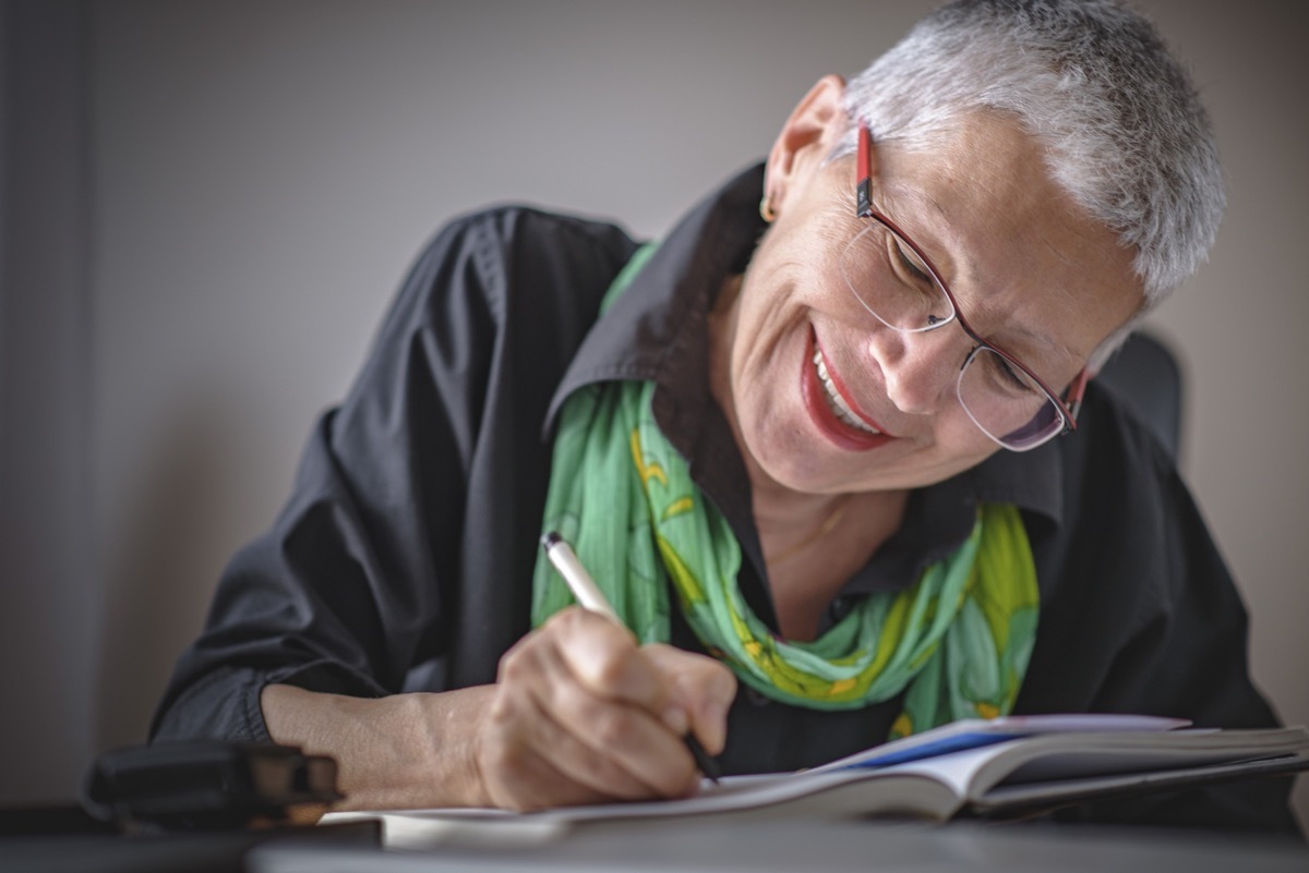 older white woman writing in a journal and smiling