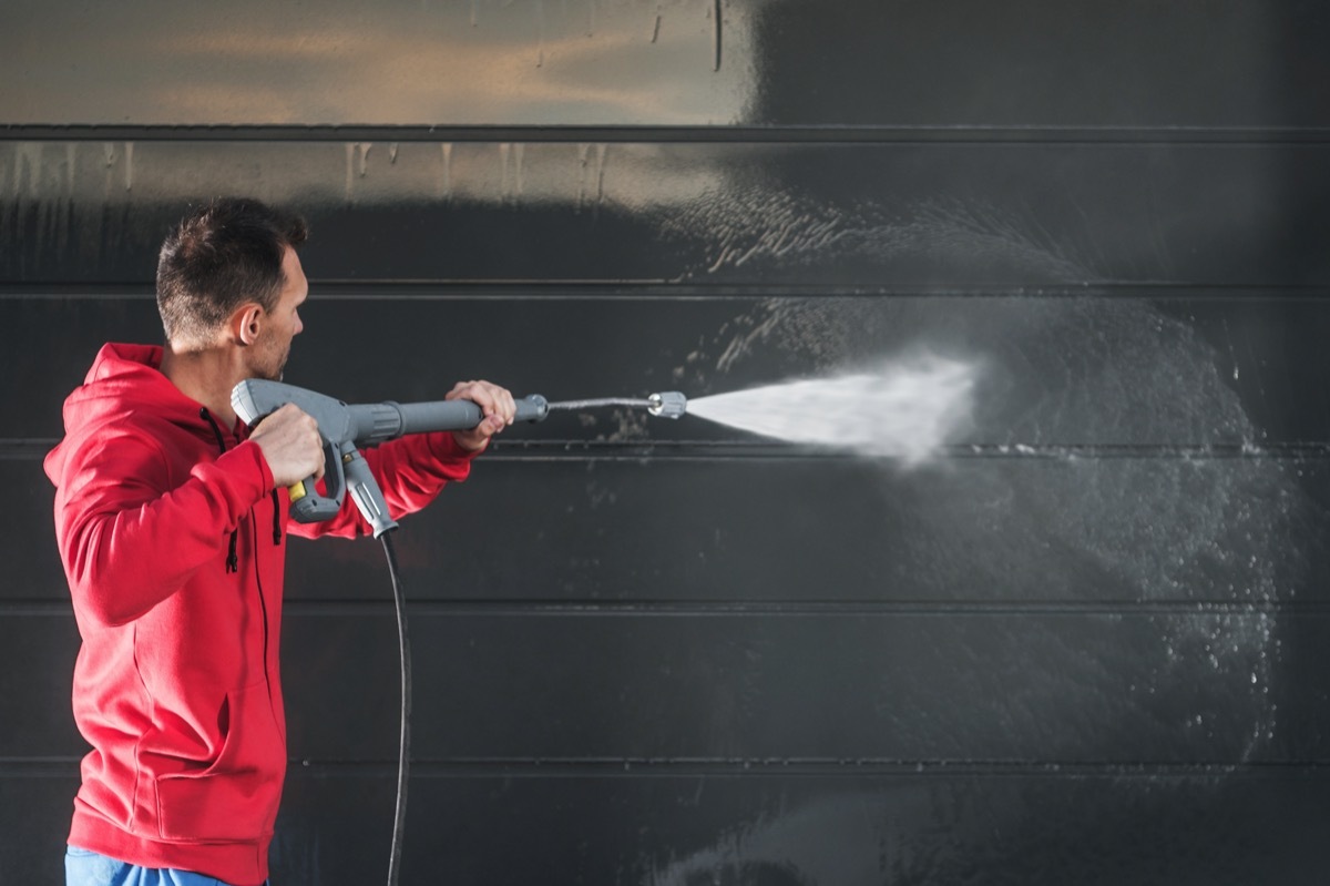 white man pressure washing dark siding