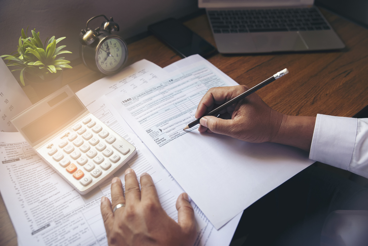 A person sits filling out tax forms with a calculator nearby