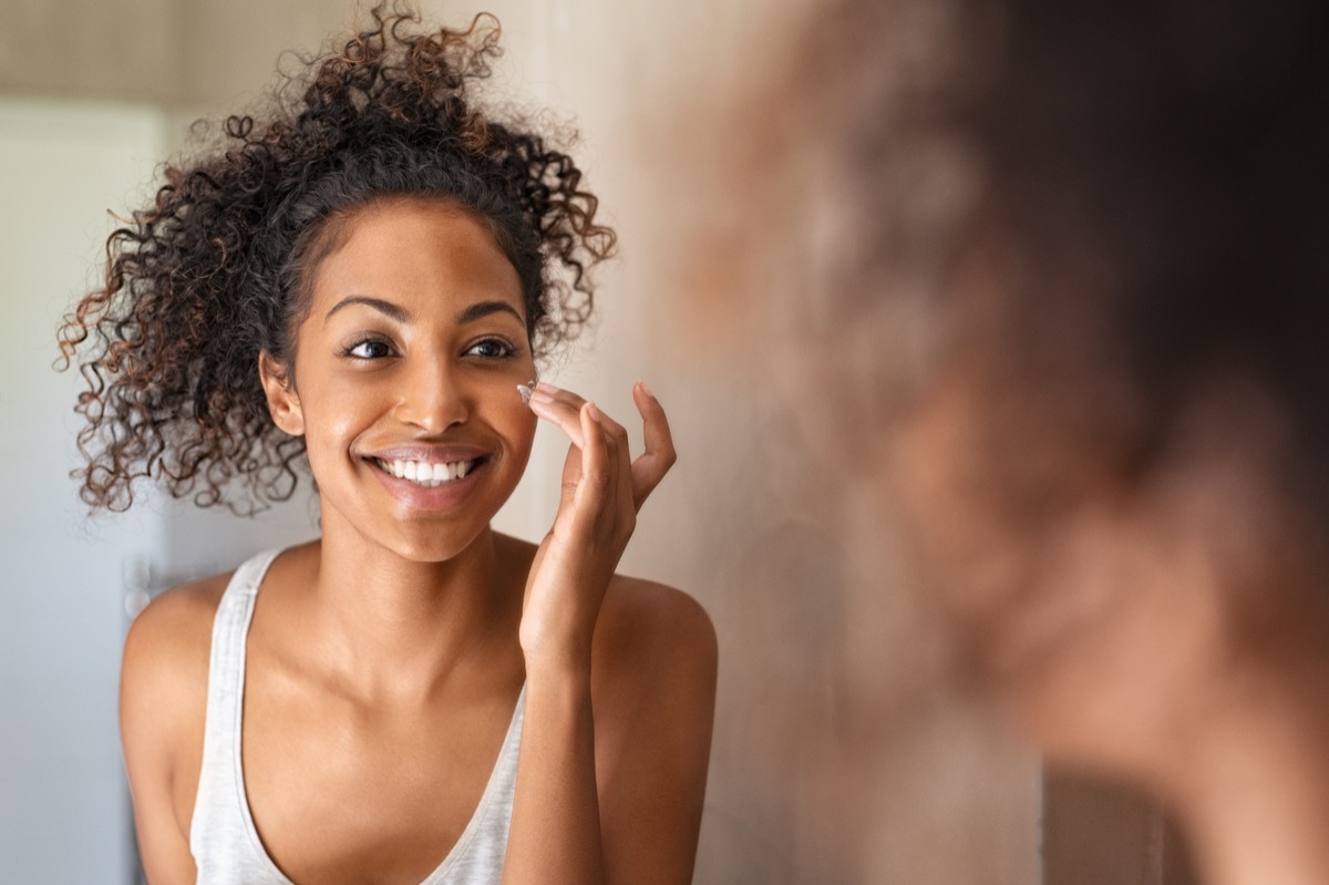 Smiling woman looking in the mirror and applying face cream