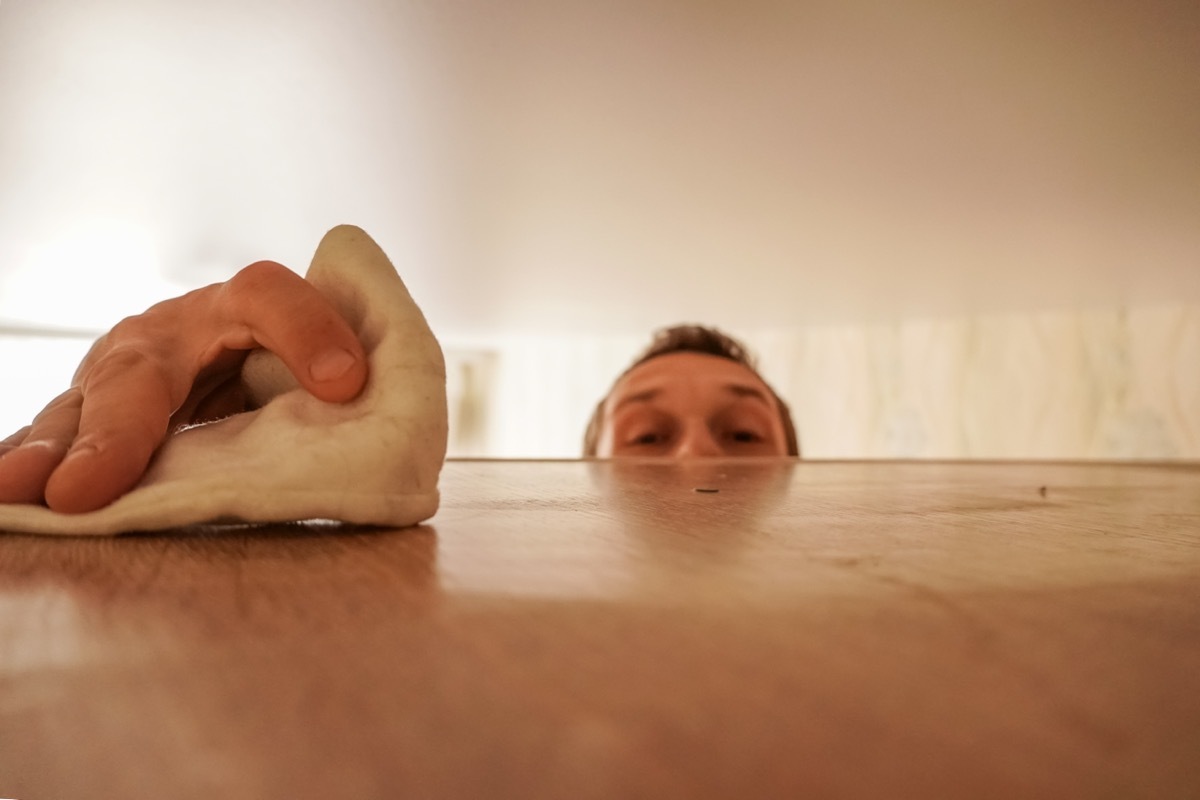 man cleaning high shelf in home