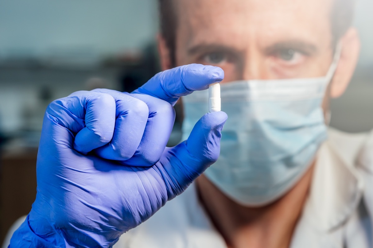 Scientist with medical mask showing white pill. Research concept. Selective focus.