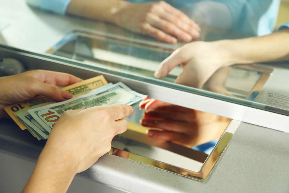 white hands passing cash under bank divider window