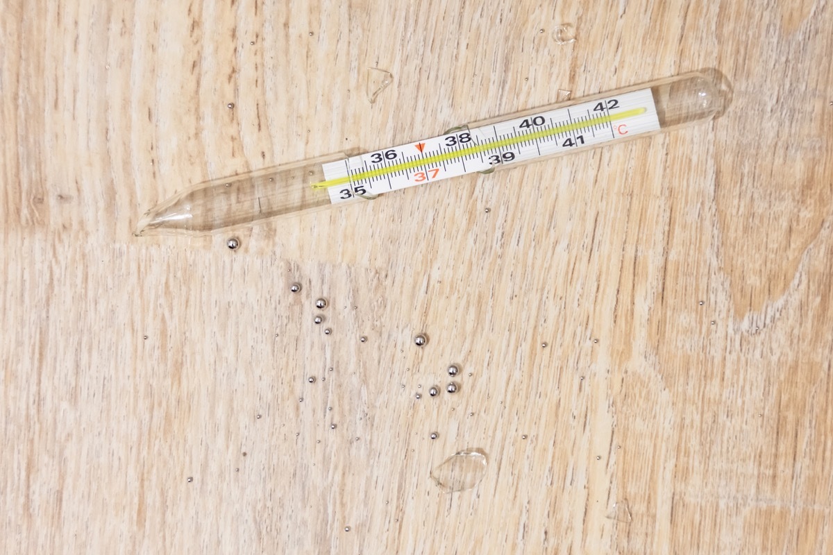 Randomly broken medical thermometer to measure a person's body temperature, glass fragments and drops of dangerous mercury on the floor