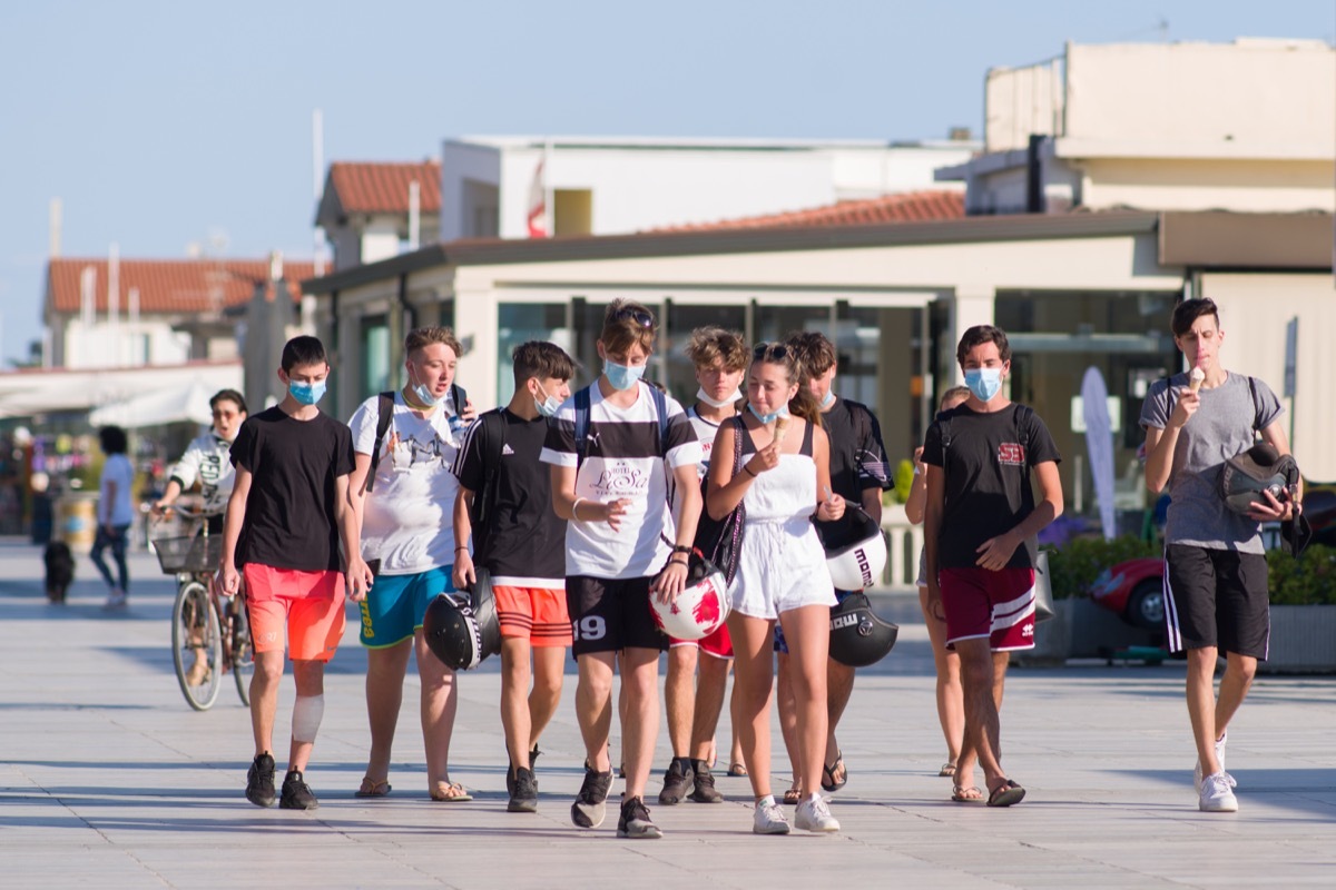 Large group of teenagers walking and eating ice cream some wearing masks some not wearing masks