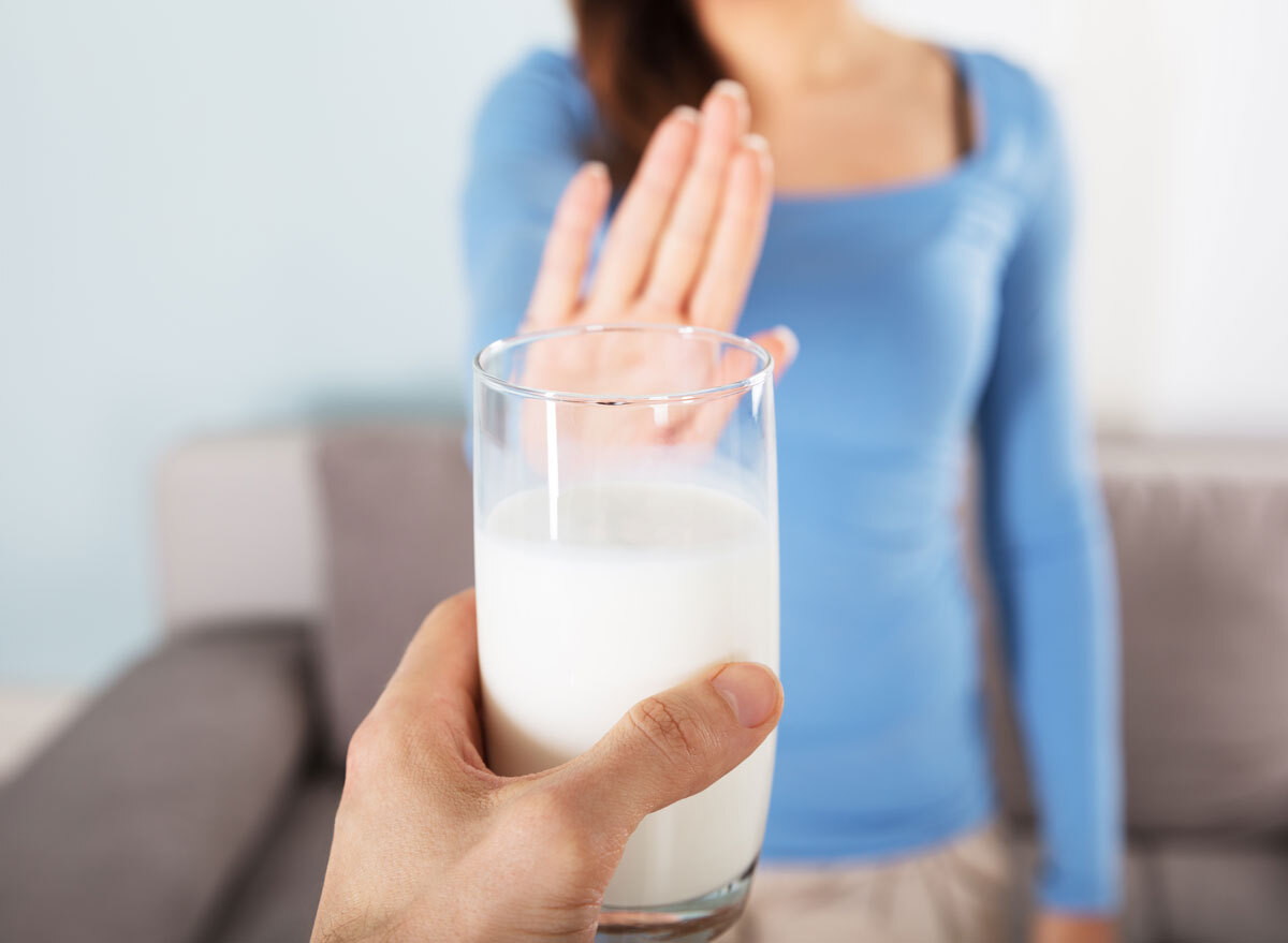 Woman holding up an outstretched hand saying no to a man offering her a glass of dairy milk