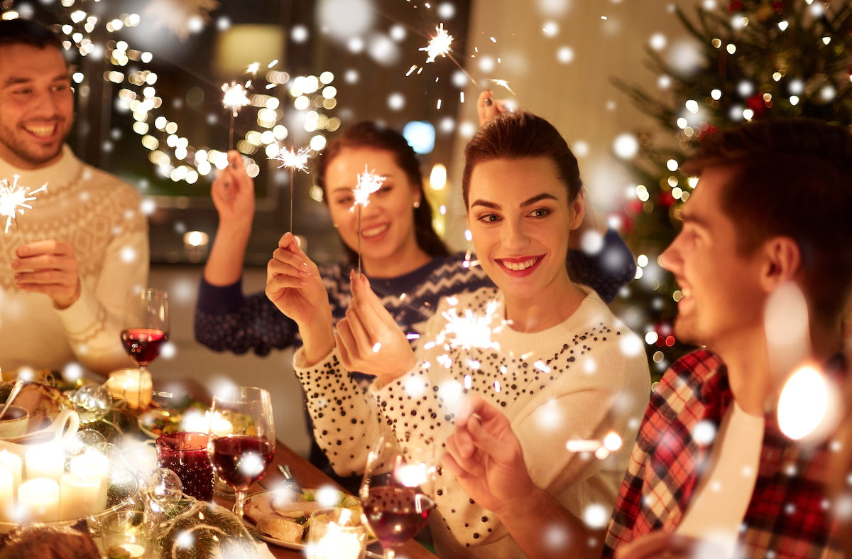 A group of happy friends at a dinner table celebrating the holidays with sparklers.