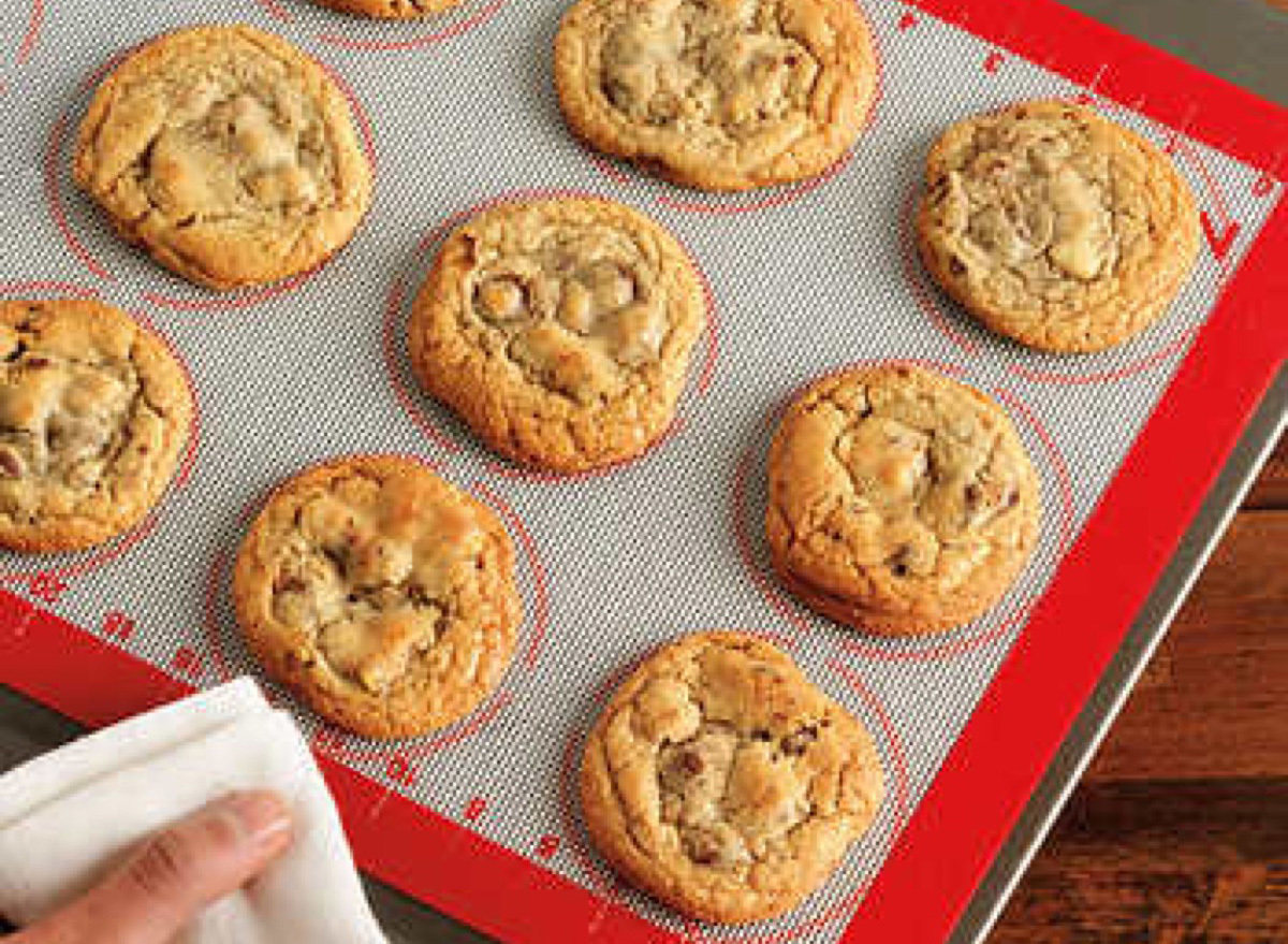 hand removing red and silver silpat with chocolate chip cookies from the oven