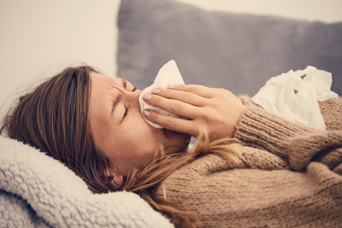 a sick woman on a couch blowing her nose with a tissue, skin cancer facts