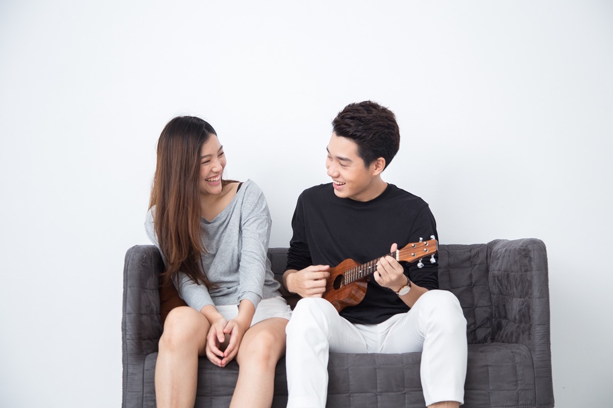 man playing a ukulele on couch next to a woman