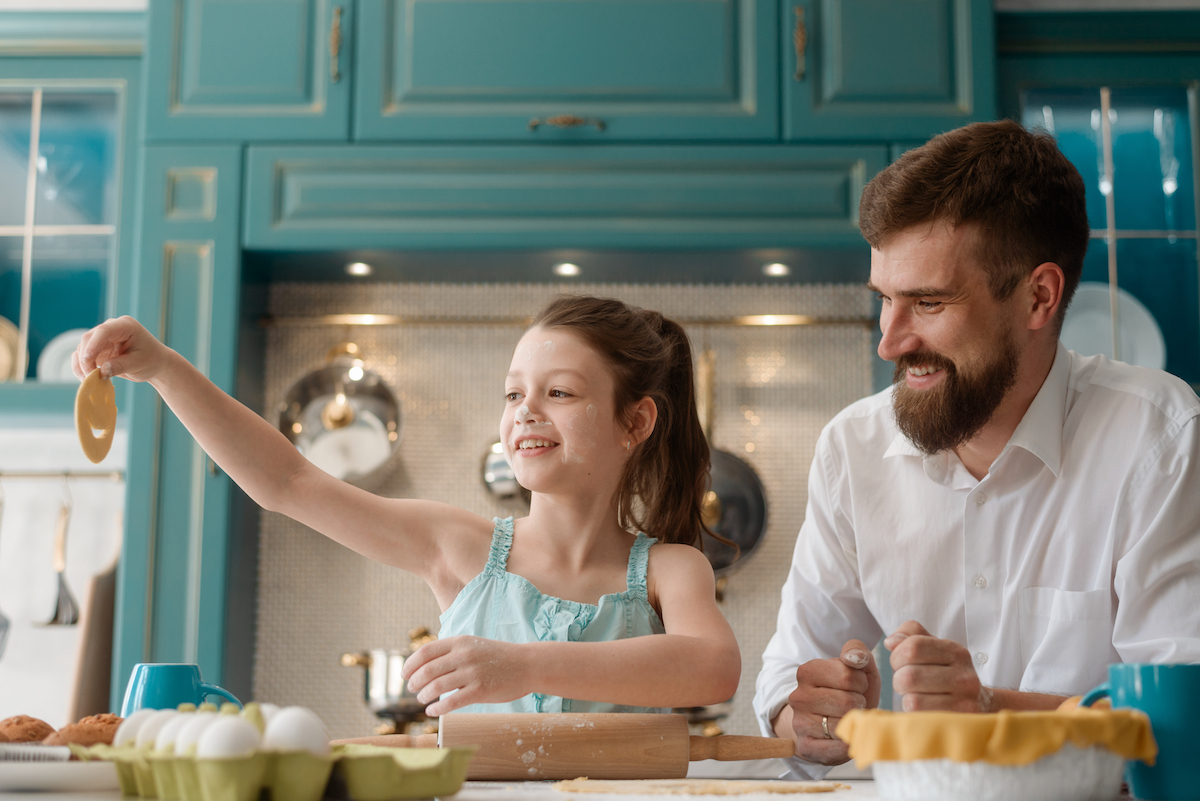 Father and daughter making cookies in their kitchen, which is a teal color.