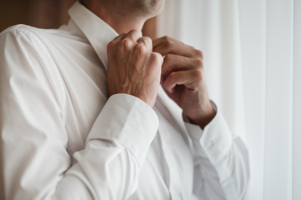 man buttoning white collar shirt