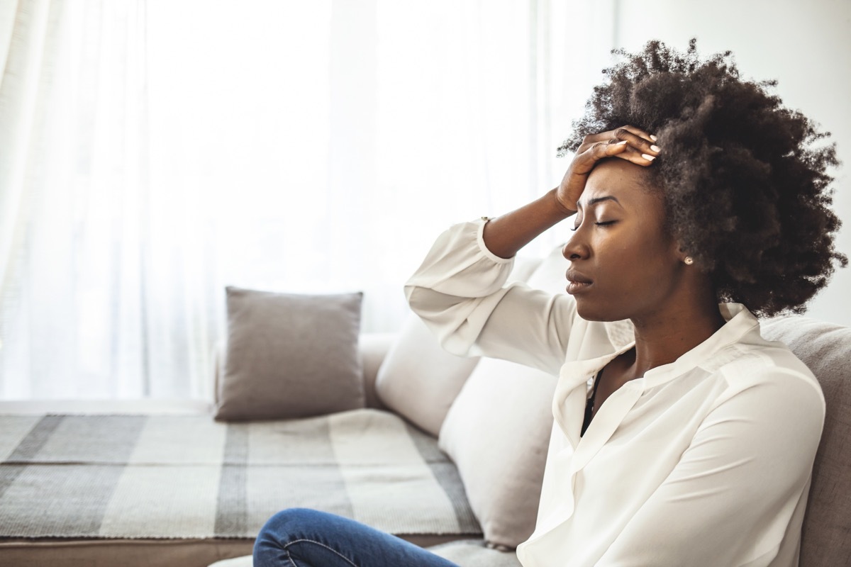 Lonely sad woman deep in thoughts sitting daydreaming or waiting for someone in the living room with a serious expression, she is pensive and suffering from insomnia sitting on couch (Lonely sad woman deep in thoughts sitting daydreaming or waiting fo