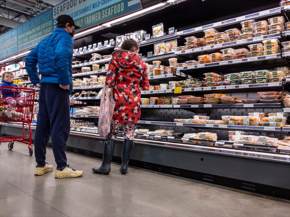 View of a man and woman with their baby, shopping at the prepared food aisle inside of a Whole Foods Market