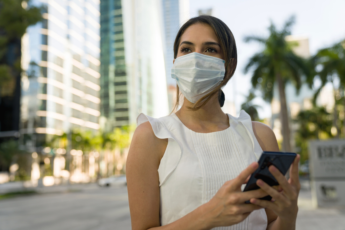 Portrait of a woman wearing a face mask on the street and checking her cell phone while outdoors during the COVID-19 pandemic