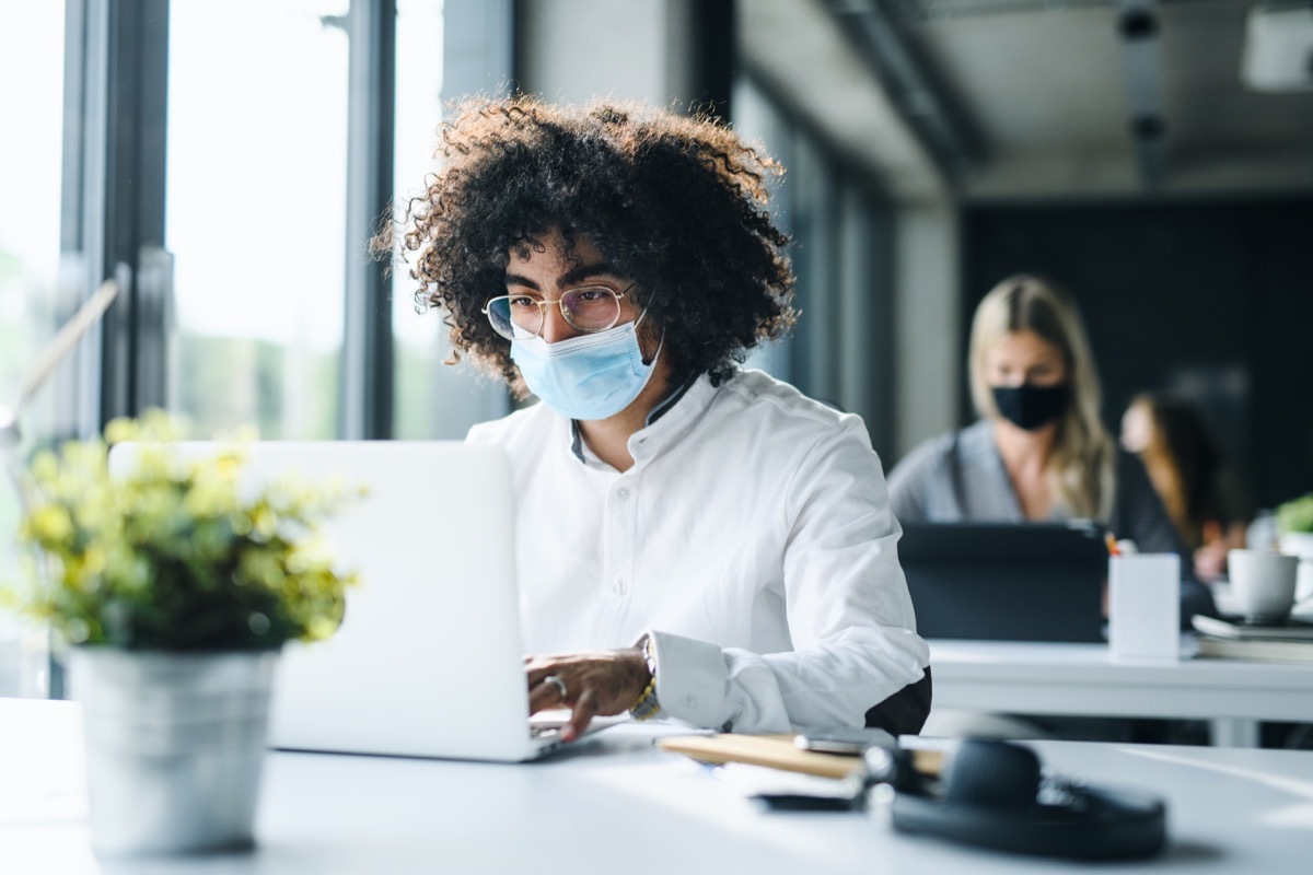 Portrait of young man with face mask back at work in office after lockdown, working.